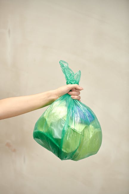 A close-up view of several black plastic rubbish bags filled and tightly knotted at the top, stacked together against a plain, light-colored wall. The bags are made of shiny, smooth plastic material a