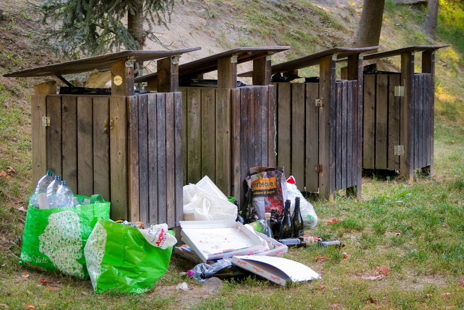 A small, light blue, vintage-style pickup truck is parked beside a pavement, loaded with an assortment of waste materials including cardboard boxes, black plastic bags, and other debris. The truck's b